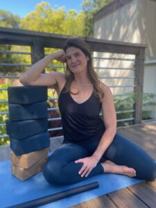 Robin Penney Movement Coach sitting in shinbox position leaning on stack of yoga blocks